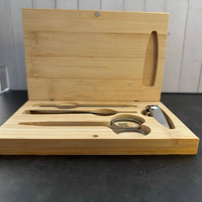 Coffret de manucure en bambou ouvert révélant quatre accessoires en acier inoxydable (ciseaux, coupe-ongles, pince, lime).