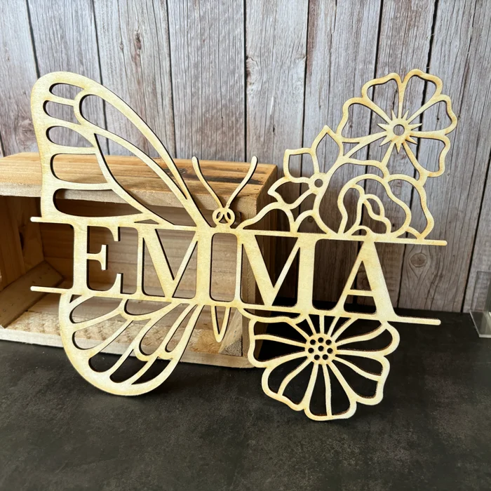 Prénom Emma découpé sur mesure en bois naturel clair intégré dans un motif ajouré d'aile de papillon et de fleurs